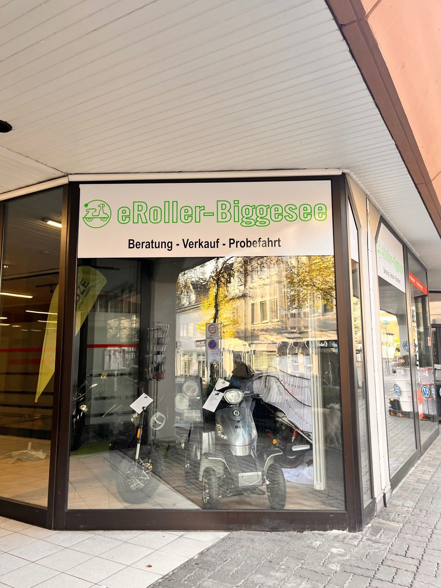 Das neue Ladenlokal von eRoller Biggesee im Geschäftszentrum Alter Rathausplatz: Schaufenster mit dem Schriftzug „eRoller-Biggesee, Beratung – Verkauf – Probefahrt“ und mehreren Elektrorollern
